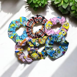 Puede incluir: Seis scrunchies de pelo coloridos con diseños de personajes de dibujos animados. Los scrunchies están hechos de tela y tienen una banda elástica fruncida.