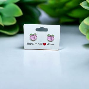 以下が含まれることがあります： 白いカードに「Handmade with love」と書かれた、桃の形をしたイヤリングのペアです。