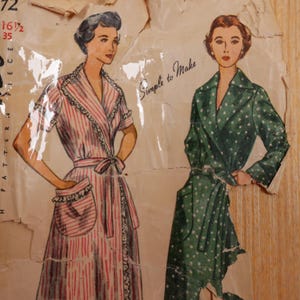 May include: A vintage sewing pattern envelope featuring two illustrations of wrap-style robes. One robe is pink and white striped with ruffled trim and a pocket, while the other is green with white polka dots. The text reads Simple to Make.