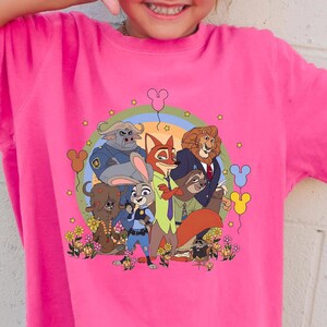 Op de afbeelding: Een felroze T-shirt met een kleurrijke afbeelding van stripfiguren, een regenboog en bloemen. De tekst "CRUNCH BERRY" staat in het wit rechtsonder op de shirt. Het shirt heeft een comfortabele pasvorm.