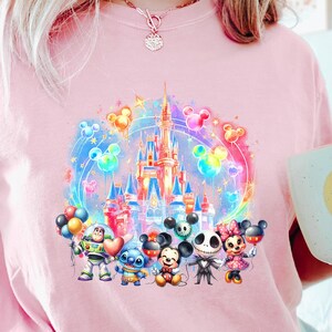 Puede incluir: Camiseta rosa con una ilustraci&oacute;n colorida del castillo de Disney, Mickey Mouse, Stitch y otros personajes. Los personajes sostienen globos y est&aacute;n parados frente al castillo.