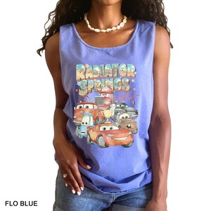 Puede incluir: Camiseta sin mangas azul claro con un gr&aacute;fico de personajes de la pel&iacute;cula Cars, con el texto "Radiator Springs". El dise&ntilde;o incluye varios coches de dibujos animados y las palabras "Flo Blue" en la parte inferior.