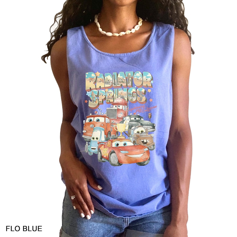 Puede incluir: Camiseta sin mangas azul claro con un gr&aacute;fico de personajes de la pel&iacute;cula Cars, con el texto "Radiator Springs". El dise&ntilde;o incluye varios coches de dibujos animados y las palabras "Flo Blue" en la parte inferior.