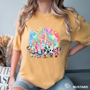 Puede incluir: Una camiseta amarilla mostaza con un gr&aacute;fico colorido del castillo de Disney, Mickey Mouse, Stitch y otros personajes. El gr&aacute;fico est&aacute; rodeado de globos coloridos.