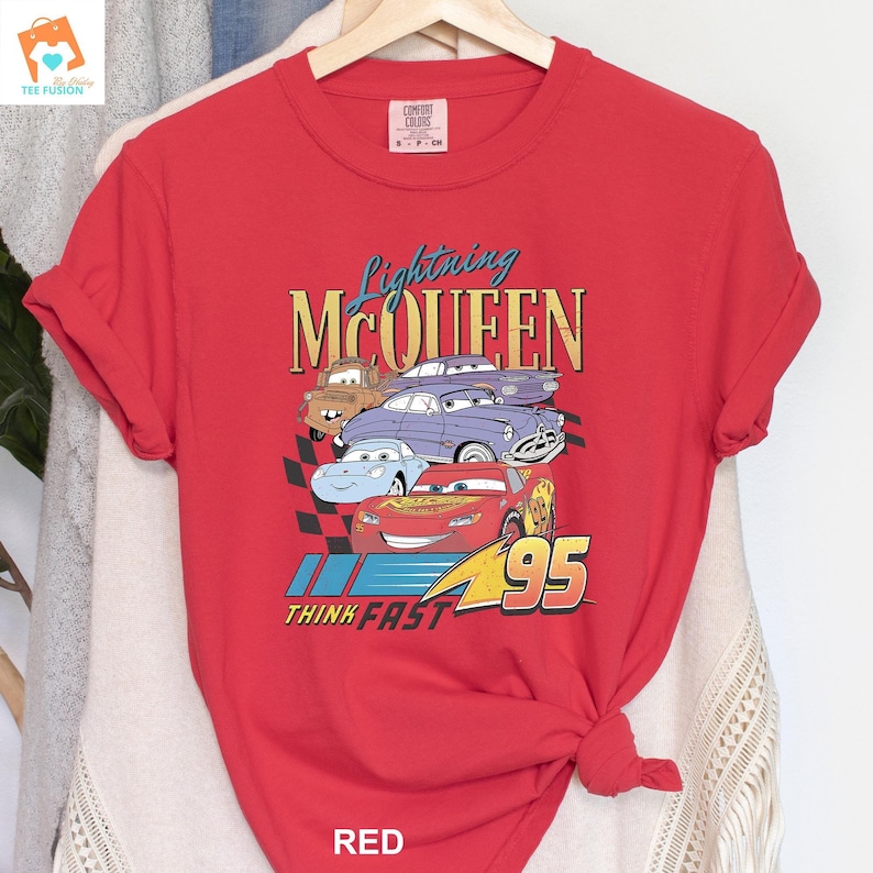May include: Red t-shirt featuring a graphic of Lightning McQueen and other Cars characters. The text "Lightning McQueen" and "Think Fast" are printed on the shirt.