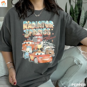 May include: A dark gray t-shirt with a graphic print of the Cars characters from the movie Cars. The graphic features the text "Radiator Springs" and "Lightning McQueen".