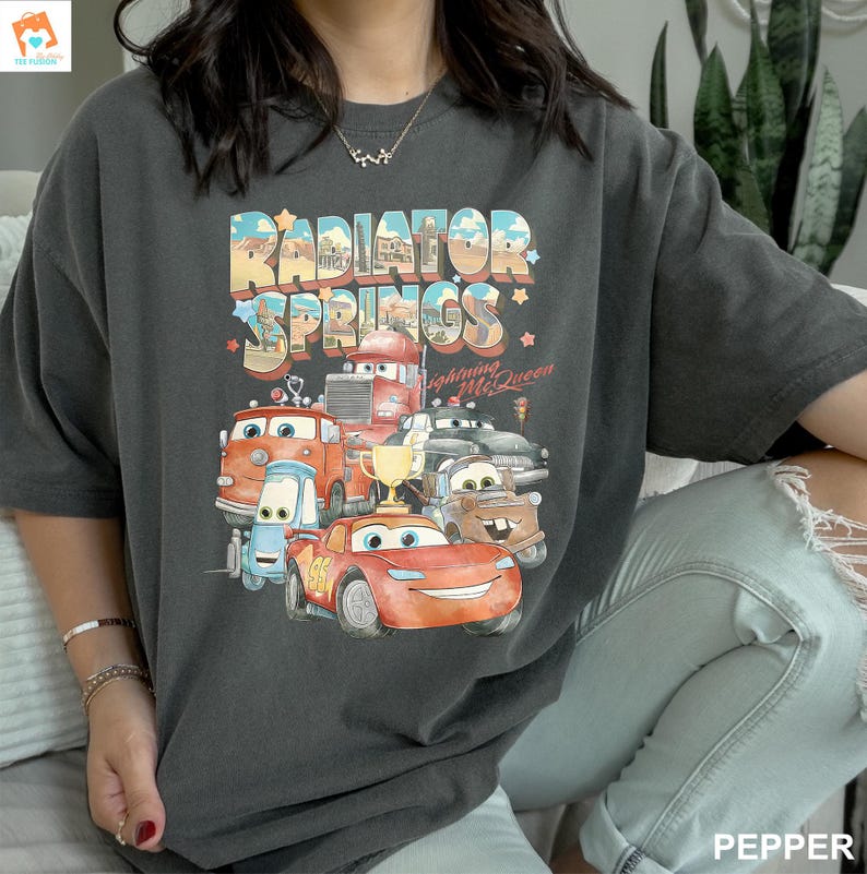 May include: A dark gray t-shirt with a graphic print of the Cars characters from the movie Cars. The graphic features the text "Radiator Springs" and "Lightning McQueen".