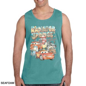 Puede incluir: Camiseta sin mangas verde mar con un gr&aacute;fico colorido de personajes de la pel&iacute;cula Cars, incluido Rayo McQueen. El texto "Radiator Springs" se muestra encima de los personajes en una fuente estilizada.