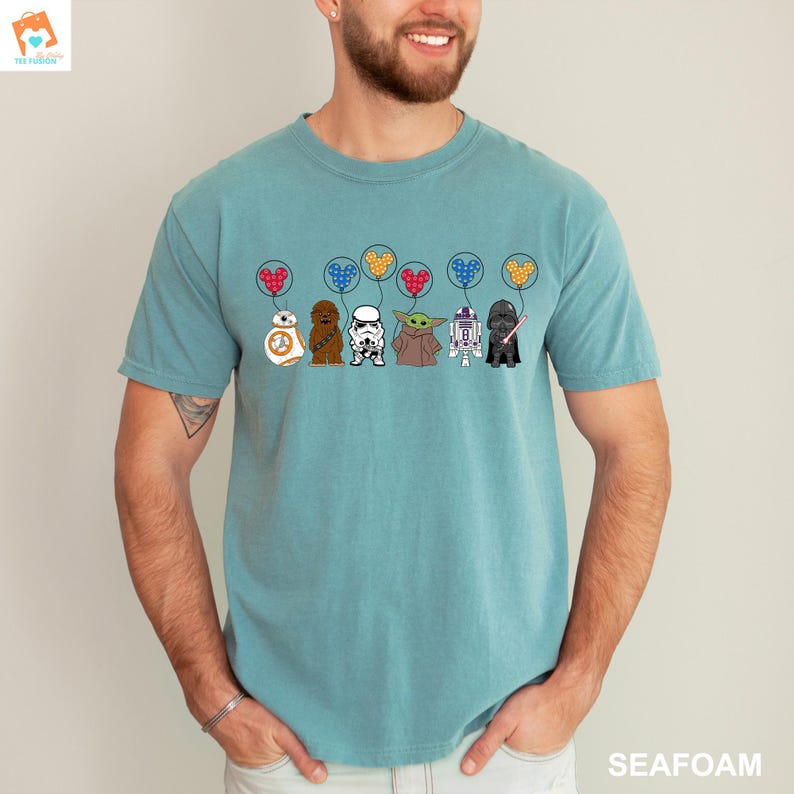 May include: A teal blue t-shirt with a graphic of Star Wars characters holding Mickey Mouse-shaped balloons. The characters include Chewbacca, Darth Vader, R2-D2, Yoda, and a Stormtrooper.