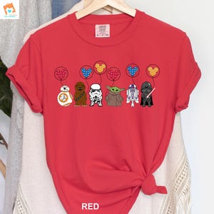 May include: Red t-shirt with a graphic of Star Wars characters holding Mickey Mouse balloons. The characters include R2-D2, Chewbacca, Stormtrooper, Baby Yoda, and Darth Vader.