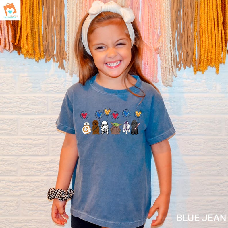 May include: A blue jean t-shirt with a graphic of Star Wars characters holding heart-shaped balloons. The characters include R2-D2, Chewbacca, Darth Vader, Yoda, and a Stormtrooper.