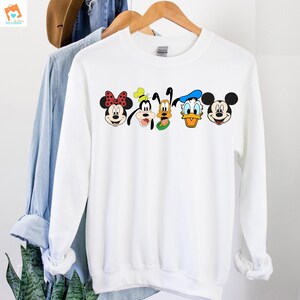 Op de afbeelding: Witte trui met een grafische print van Mickey Mouse, Minnie Mouse, Donald Duck, Goofy en Pluto. De personages lachen allemaal en hebben hun kenmerkende kenmerken.