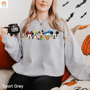 Op de afbeelding: Een grijs sweatshirt met een print van Mickey Mouse, Minnie Mouse, Donald Duck, Goofy en Pluto. De personages zijn in een rij over de voorkant van het sweatshirt geplaatst.
