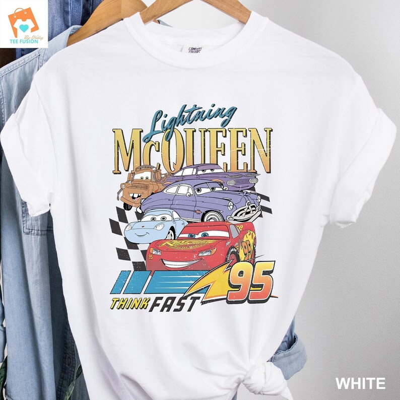 May include: White t-shirt featuring a graphic of Lightning McQueen and other Cars characters. The text "Lightning McQueen" is in yellow and the text "Think Fast" is in blue. The number "95" is in red.