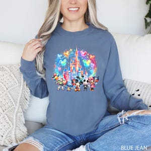 Puede incluir: Una sudadera azul con una ilustraci&oacute;n colorida de Mickey Mouse, Minnie Mouse, Stitch y Jack Skellington frente al Castillo de Cenicienta con globos. El texto "BLUE JEAN" est&aacute; en la parte inferior de la imagen.