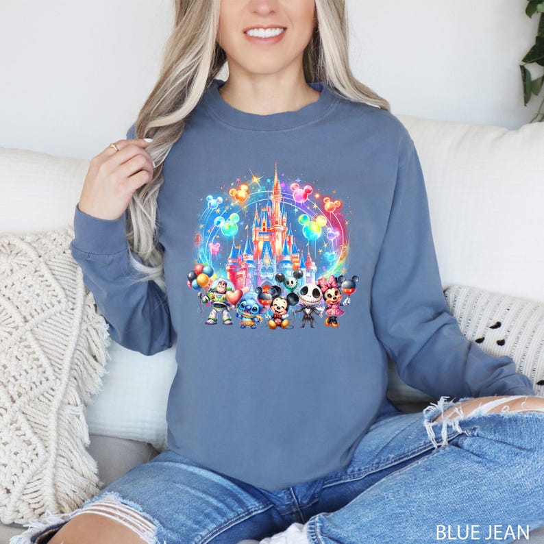 Puede incluir: Una sudadera azul con una ilustraci&oacute;n colorida de Mickey Mouse, Minnie Mouse, Stitch y Jack Skellington frente al Castillo de Cenicienta con globos. El texto "BLUE JEAN" est&aacute; en la parte inferior de la imagen.