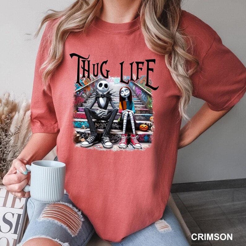 Puede incluir: Una camiseta roja con un gr&aacute;fico de Jack Skellington y Sally de Pesadilla antes de Navidad sentados en un tramo de escaleras con el texto "Thug Life" encima.