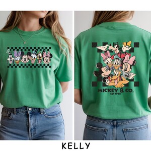 May include: A bright green t-shirt featuring a graphic of Disney characters including Mickey Mouse, Minnie Mouse, Donald Duck, Daisy Duck, Goofy, and Pluto. The front shows a horizontal checkered strip, while the back displays a larger group graphic with the text MICKEY & CO. EST 1928.