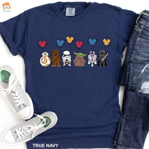 May include: A navy blue t-shirt with a graphic of Star Wars characters holding Mickey Mouse balloons. The characters include Chewbacca, Darth Vader, R2-D2, a Stormtrooper, and Baby Yoda.