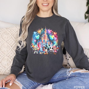 Puede incluir: Una sudadera gris oscuro con un estampado gr&aacute;fico colorido de un castillo de Disney rodeado de globos de Mickey Mouse. El gr&aacute;fico tambi&eacute;n incluye personajes como Stitch, Woody y Jack Skellington.