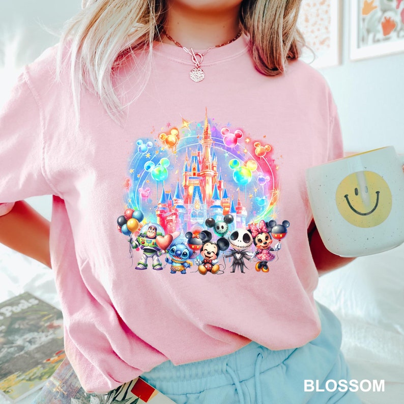 Puede incluir: Camiseta rosa con una ilustraci&oacute;n colorida del castillo de Disney, Mickey Mouse, Stitch y otros personajes. Los personajes sostienen globos y est&aacute;n parados frente al castillo.
