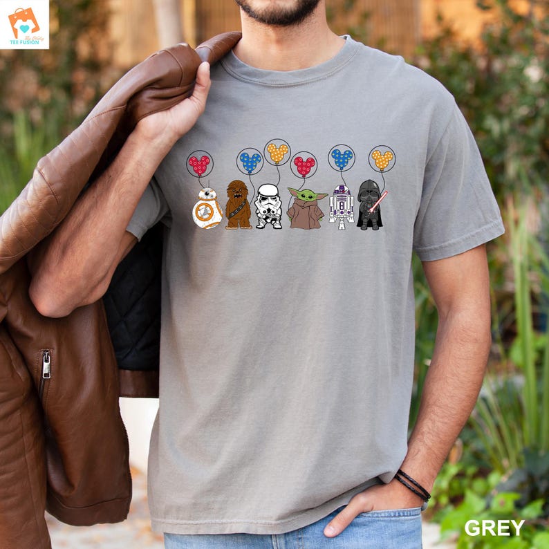 May include: A grey t-shirt with a graphic of Star Wars characters holding balloons shaped like Mickey Mouse ears. The characters include Chewbacca, Stormtrooper, Yoda, R2-D2, and Darth Vader. The balloons are red, blue, yellow, and green.