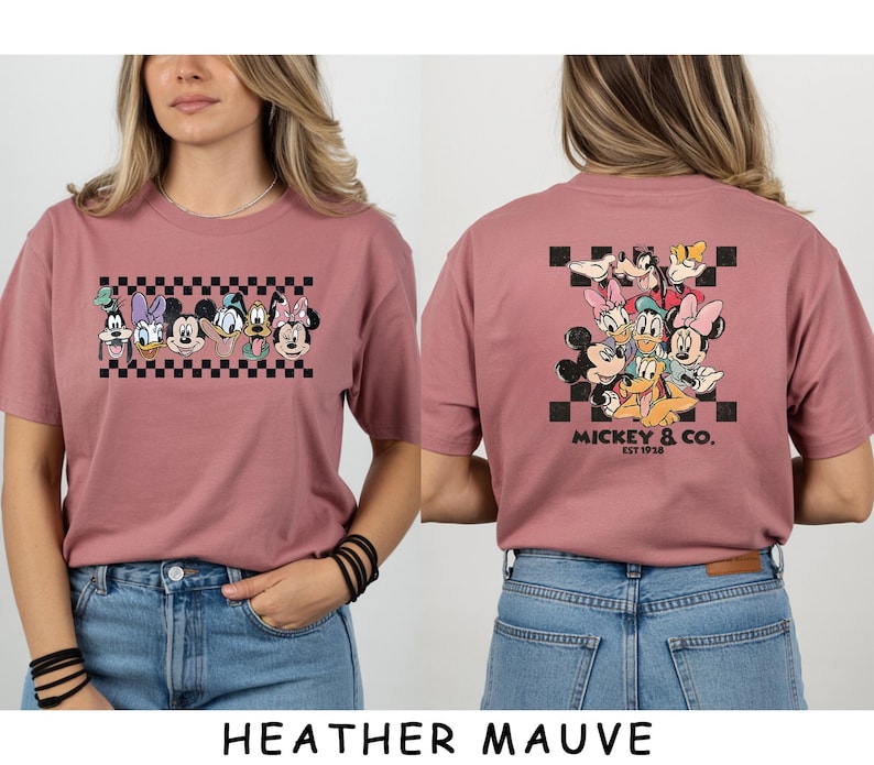 May include: A heather mauve t-shirt featuring a front graphic of Disney characters in a row above a black and white checkerboard pattern and a back graphic of the same characters clustered together with the text Mickey & Co. Est 1928.