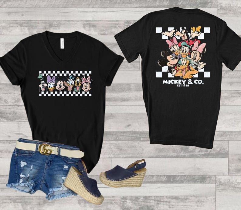 May include: A black V-neck t-shirt featuring a graphic of Disney characters over a white and black checkered pattern on the front and back. The back design includes the text MICKEY & CO. EST 1928. Also includes blue denim shorts and navy wedge sandals.