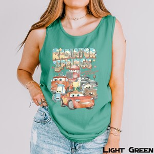 Puede incluir: Camiseta sin mangas verde claro con un gr&aacute;fico colorido de personajes de la pel&iacute;cula Cars, incluido Rayo McQueen, con el texto "Radiator Springs". El dise&ntilde;o incluye un trofeo y varios veh&iacute;culos.