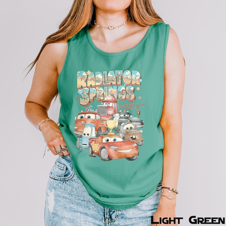 Puede incluir: Camiseta sin mangas verde claro con un gr&aacute;fico colorido de personajes de la pel&iacute;cula Cars, incluido Rayo McQueen, con el texto "Radiator Springs". El dise&ntilde;o incluye un trofeo y varios veh&iacute;culos.