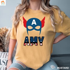 May include: A yellow t-shirt with a red, white, and blue Captain America mask and the name "AMY" in red, white, and blue letters.