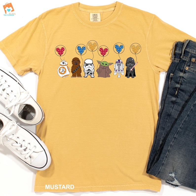 May include: A yellow t-shirt with a graphic of Star Wars characters holding balloons shaped like Mickey Mouse heads. The characters include R2-D2, Chewbacca, Darth Vader, a Stormtrooper, and Baby Yoda.