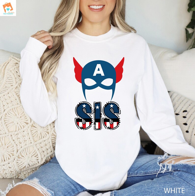 May include: White long-sleeved shirt with a blue and red American flag design. The design features a blue Captain America mask with a red, white, and blue star on the forehead and the word "SIS" in red, white, and blue letters.
