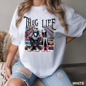 Puede incluir: Camiseta blanca con un estampado gr&aacute;fico de Jack Skellington y Sally de Pesadilla antes de Navidad sentados en un tramo de escaleras con el texto "Thug Life" encima.