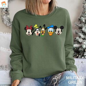 Op de afbeelding: Een groen sweatshirt met een print van Mickey Mouse, Minnie Mouse, Donald Duck, Goofy en Pluto. Het sweatshirt heeft een ronde hals en lange mouwen.
