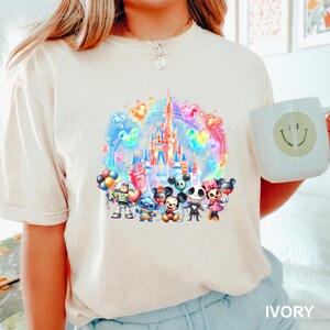 Puede incluir: Una camiseta blanca con una ilustraci&oacute;n colorida de un castillo de Disney, Mickey Mouse, Stitch y otros personajes. El texto "IVORY" est&aacute; en la esquina inferior derecha de la imagen.