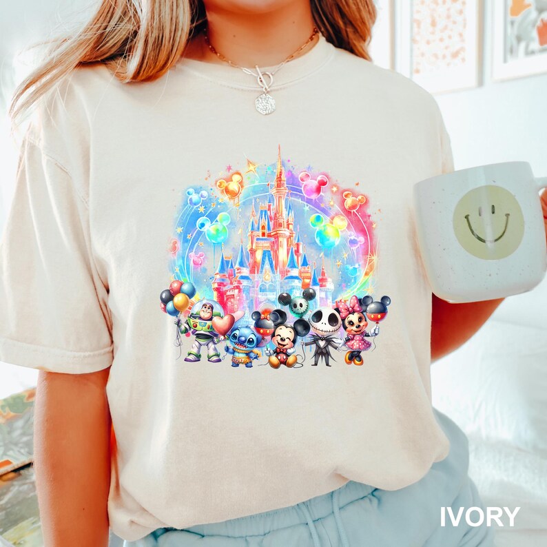 Puede incluir: Una camiseta blanca con una ilustraci&oacute;n colorida de un castillo de Disney, Mickey Mouse, Stitch y otros personajes. El texto "IVORY" est&aacute; en la esquina inferior derecha de la imagen.