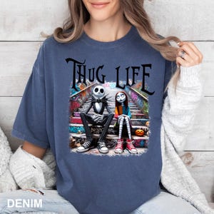 Puede incluir: Una camiseta azul oscuro con un gr&aacute;fico de Jack Skellington y Sally de Pesadilla Antes de Navidad sentados en una escalera cubierta de grafiti. El texto "THUG LIFE" est&aacute; impreso encima de ellos.