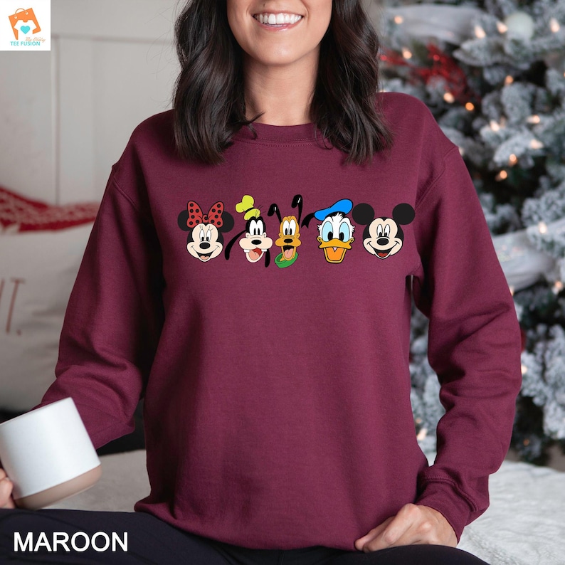 Op de afbeelding: Een maroon sweatshirt met een grafische print van Mickey Mouse, Minnie Mouse, Donald Duck, Goofy en Pluto. De personages zijn in een rij over de voorkant van het sweatshirt geplaatst.