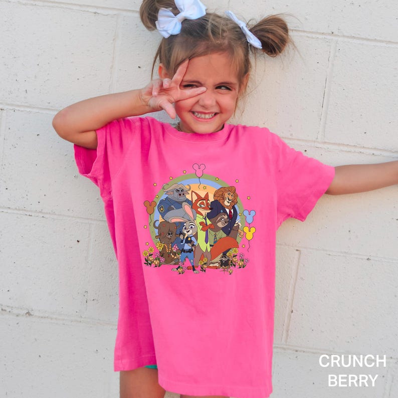 Op de afbeelding: Een felroze T-shirt met een kleurrijke afbeelding van stripfiguren, een regenboog en bloemen. De tekst "CRUNCH BERRY" staat in het wit rechtsonder op de shirt. Het shirt heeft een comfortabele pasvorm.