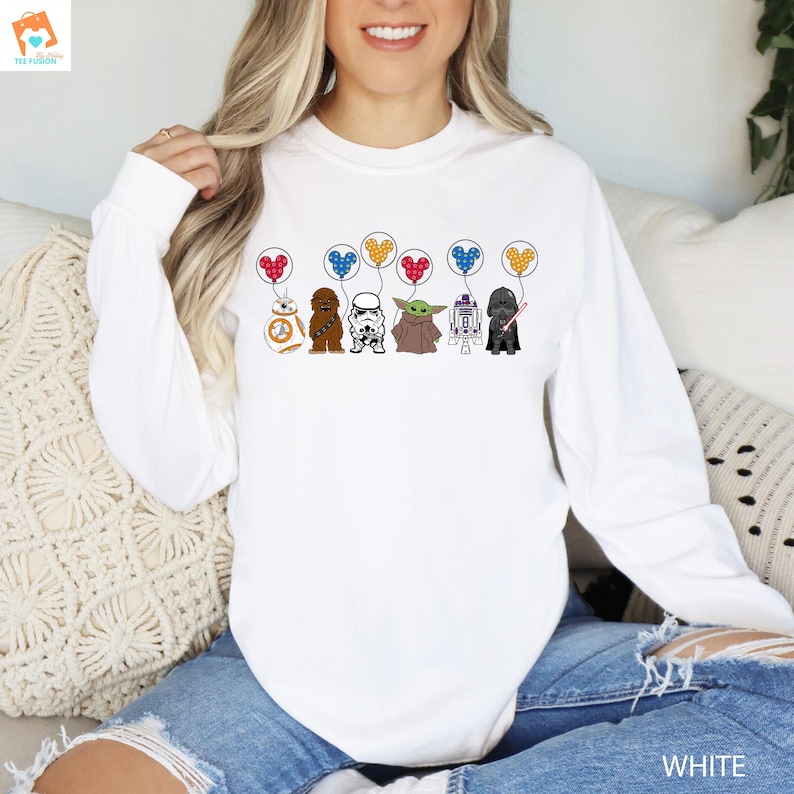 May include: White long-sleeve sweatshirt with a graphic of Star Wars characters holding balloons shaped like Mickey Mouse ears. The characters include Chewbacca, R2-D2, Darth Vader, and Yoda.