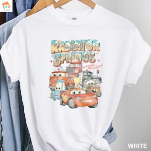 May include: White t-shirt with a graphic print of the Cars characters from the movie Cars. The graphic features the text "Radiator Springs" and the characters Lightning McQueen and Mater.