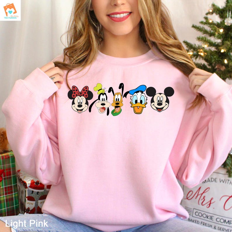 Op de afbeelding: Een lichtroze sweatshirt met een afbeelding van Mickey Mouse, Minnie Mouse, Donald Duck, Goofy en Pluto. De personages staan in een rij en glimlachen.