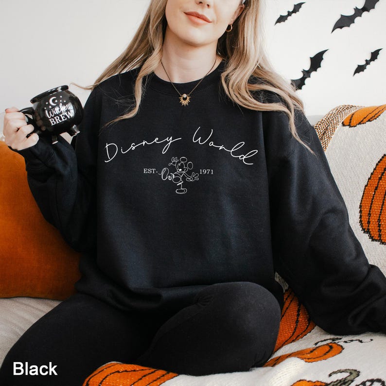 May include: Black crewneck sweatshirt with the text "Disney World" in a script font, with a Mickey Mouse graphic and the text "EST. 1971". The word "Black" is at the bottom left of the image.