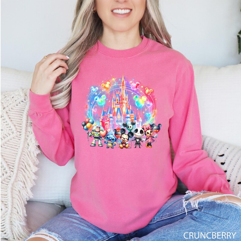 Puede incluir: Sudadera rosa de manga larga con un estampado gr&aacute;fico colorido de Mickey Mouse, Minnie Mouse, Stitch y otros personajes de Disney frente al Castillo de Cenicienta con globos.