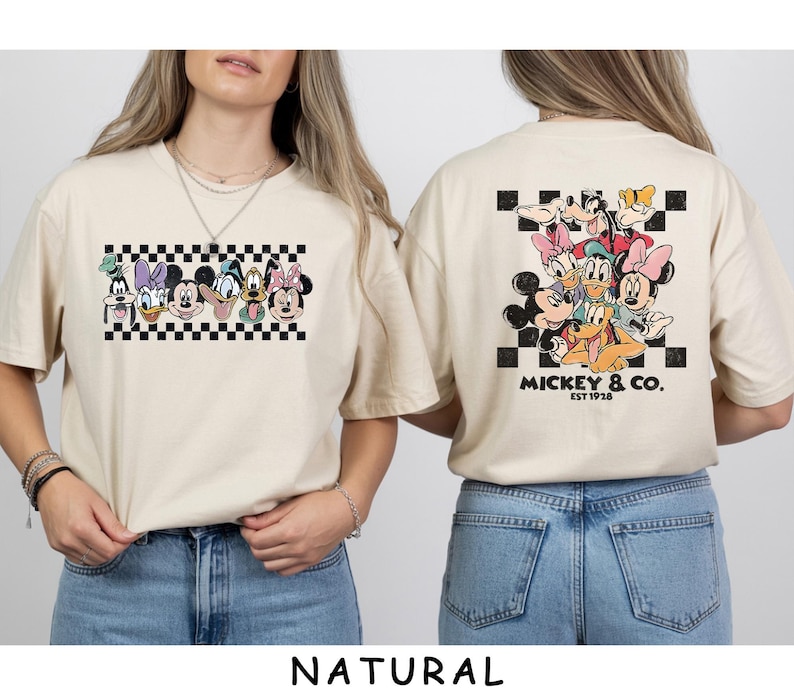 May include: A natural-colored t-shirt featuring a graphic of Disney characters including Mickey, Minnie, Donald, Daisy, Goofy, and Pluto. The front shows the characters in a row over a black and white checkerboard pattern. The back features the same characters grouped together above the text Mickey & Co. Est 1928.