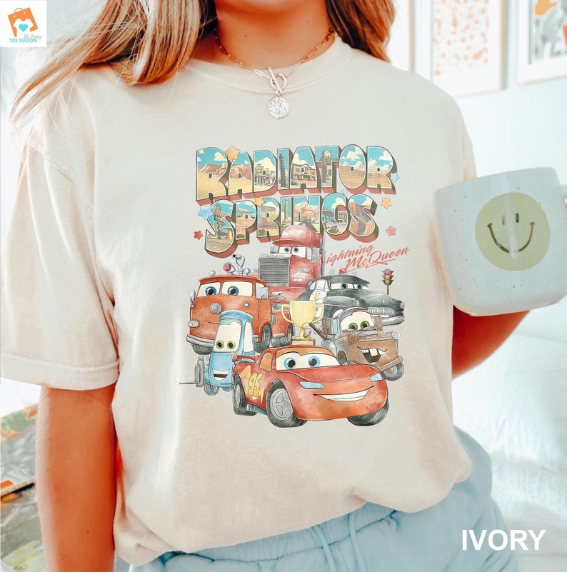 May include: Ivory t-shirt with a graphic of the Cars characters from the movie Cars. The graphic includes the text "Radiator Springs" and "Lightning McQueen".
