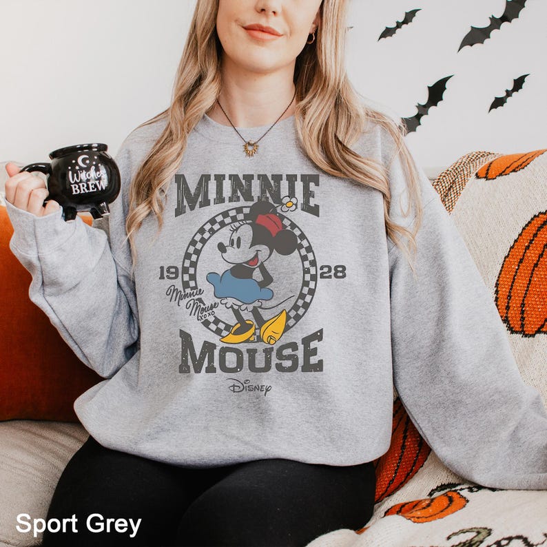 Puede incluir: Una sudadera gris con un gr&aacute;fico de estilo vintage de Minnie Mouse. El gr&aacute;fico presenta a Minnie Mouse en un c&iacute;rculo a cuadros con el texto "Minnie Mouse" y "Disney" debajo.