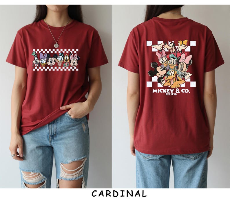 May include: A cardinal red short-sleeve t-shirt featuring a graphic of Disney characters on the front and back. The front shows a row of character faces over a white and red checkerboard pattern. The back displays the same characters with the text MICKEY & CO. EST 1928.