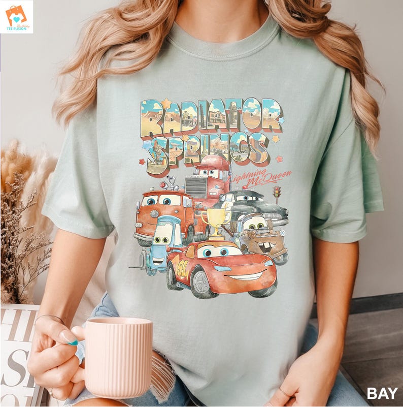 May include: A light blue t-shirt with a graphic of the Cars characters from the Disney Pixar movie Cars. The graphic features the text "Radiator Springs" and "Lightning McQueen".